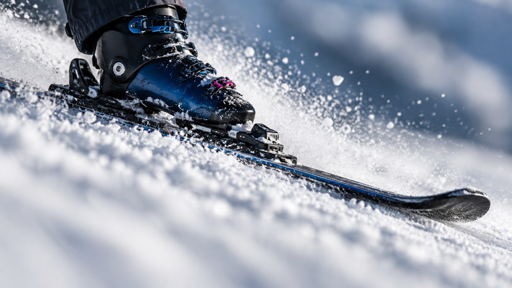 A close-up of a ski edge and boot carving through snow